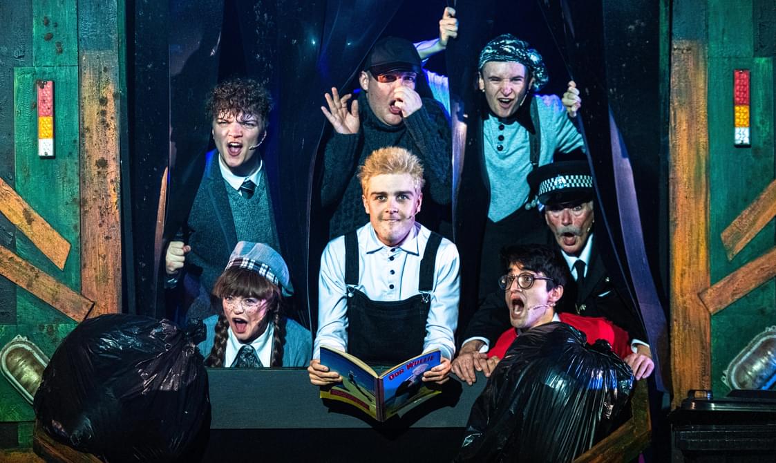 A promotional image from a theatrical production of 'Oor Wullie' showing six actors on stage.